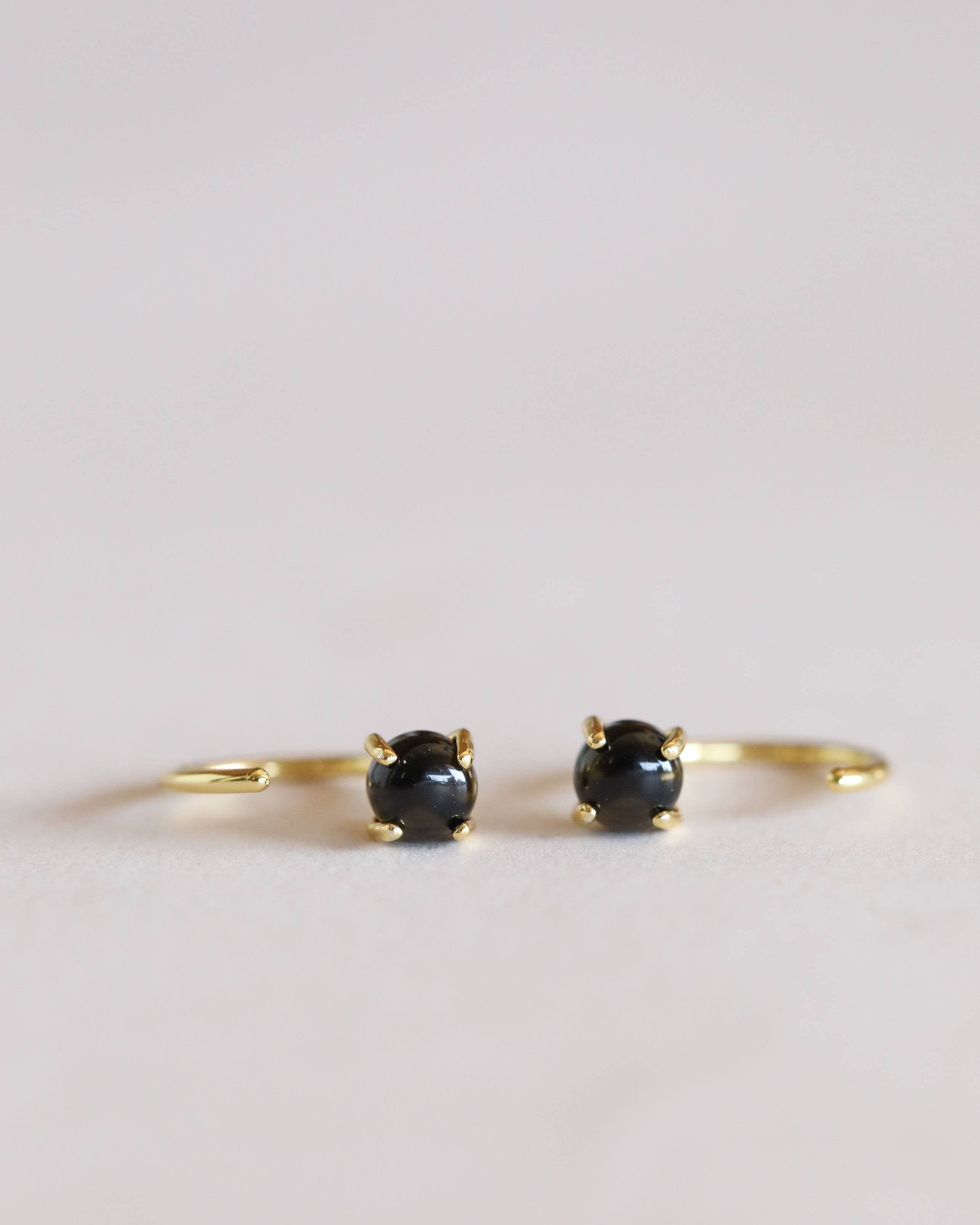 Pair of gold hoop earrings with black gemstones on a light gray background