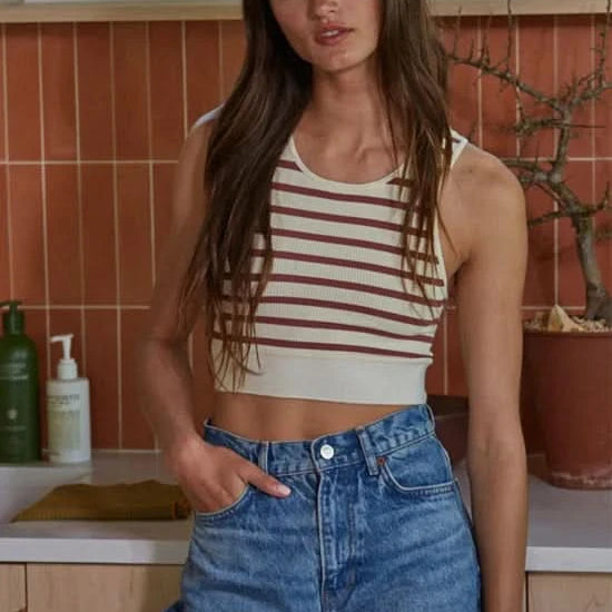 Woman wearing a crème and red striped sleeveless U-V neckline tank top with blue jeans.