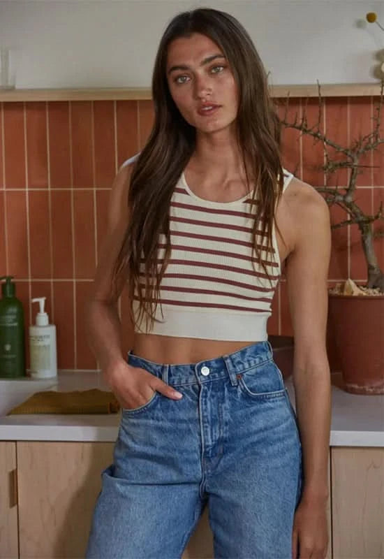 Woman wearing a crème and red striped sleeveless U-V neckline tank top with blue jeans.