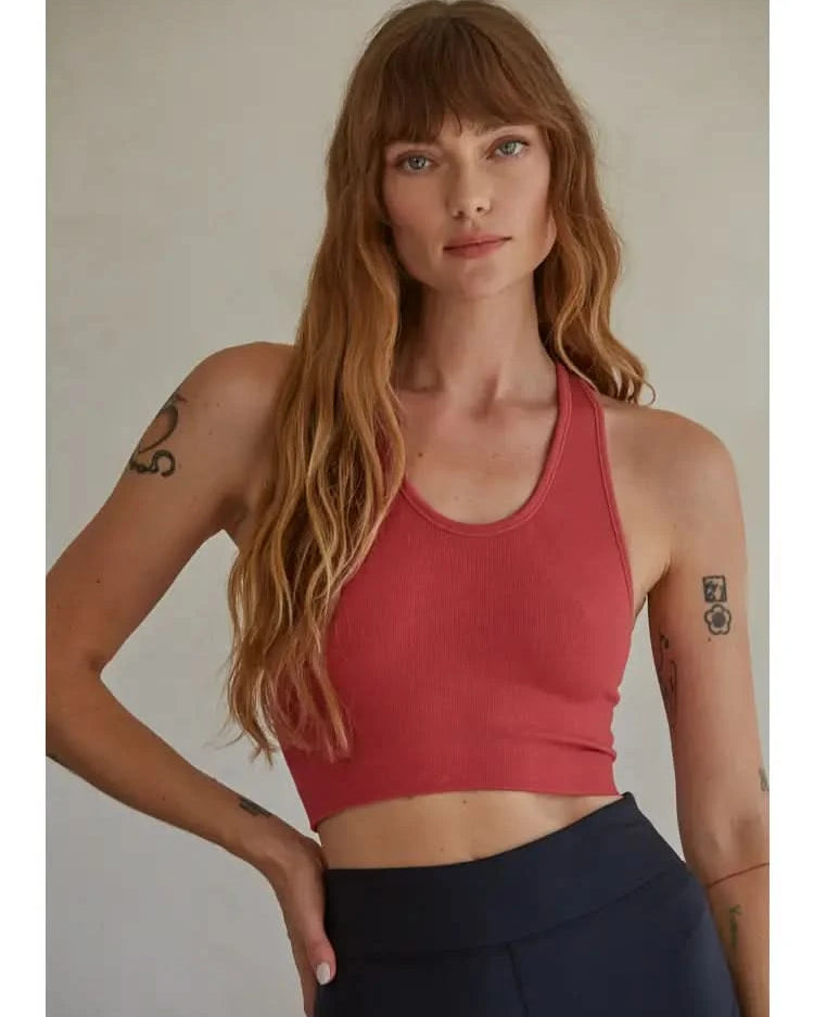 Woman wearing a red knit seamless ribbed scoop with a U-V neckline tank top with black pants standing in front of a blank background.
