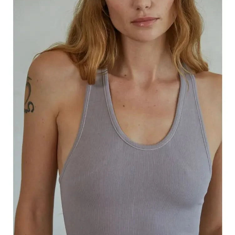 Woman wearing a mauve knit seamless ribbed scoop with a U-V neckline tank top standing in front of a blank background.