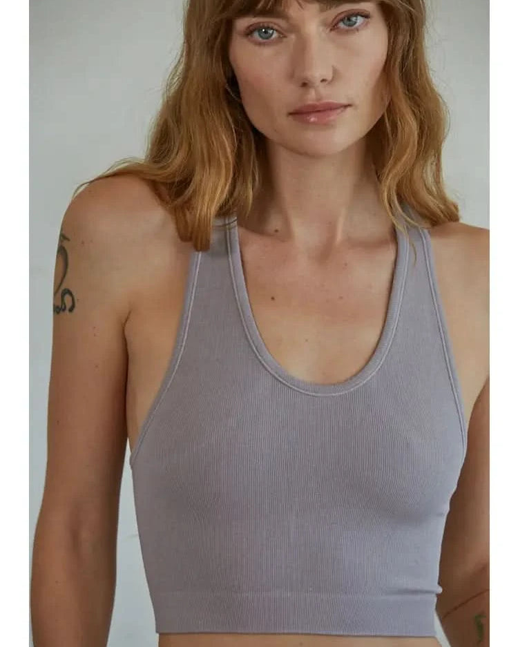 Woman wearing a mauve knit seamless ribbed scoop with a U-V neckline tank top standing in front of a blank background.