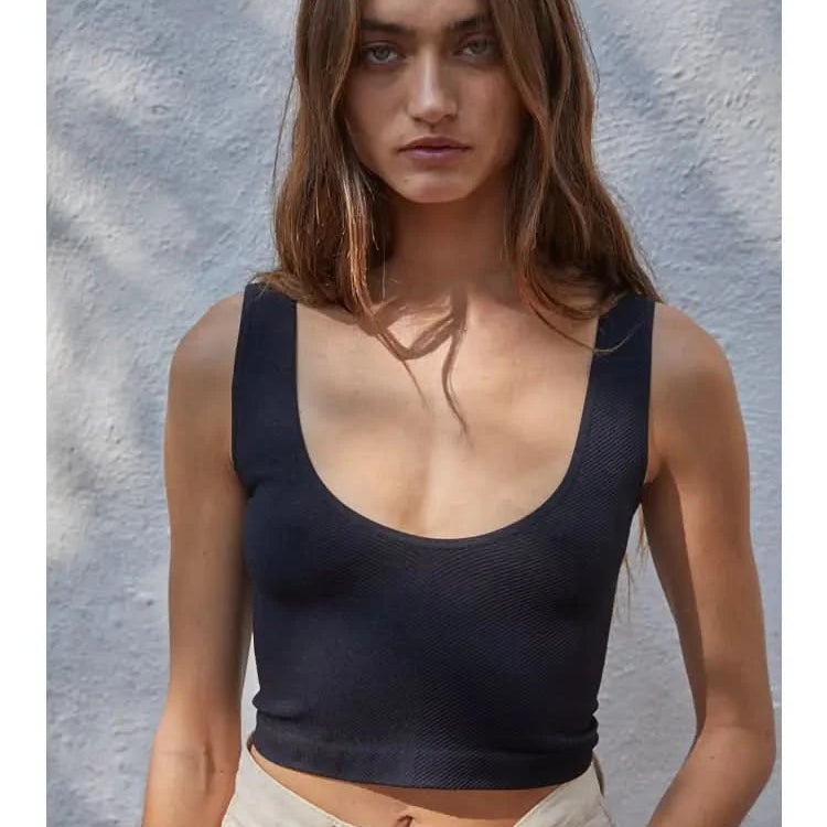 Woman wearing a black knit seamless chevron design with a sleeveless U-V neckline tank top behind a white wall.