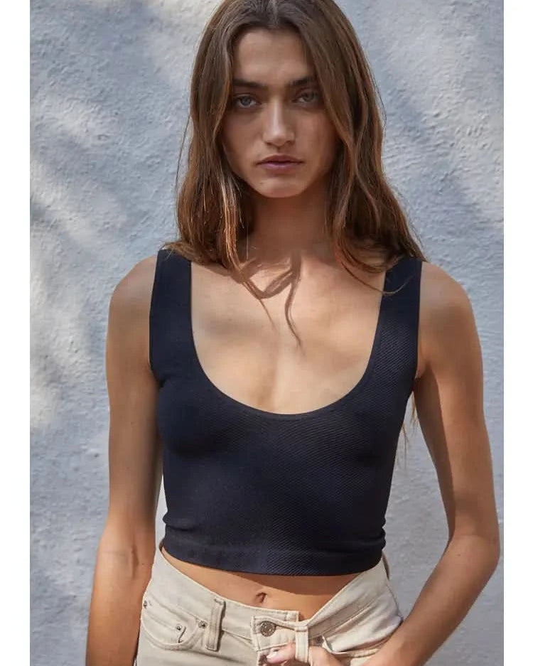 Woman wearing a black knit seamless chevron design with a sleeveless U-V neckline tank top behind a white wall.