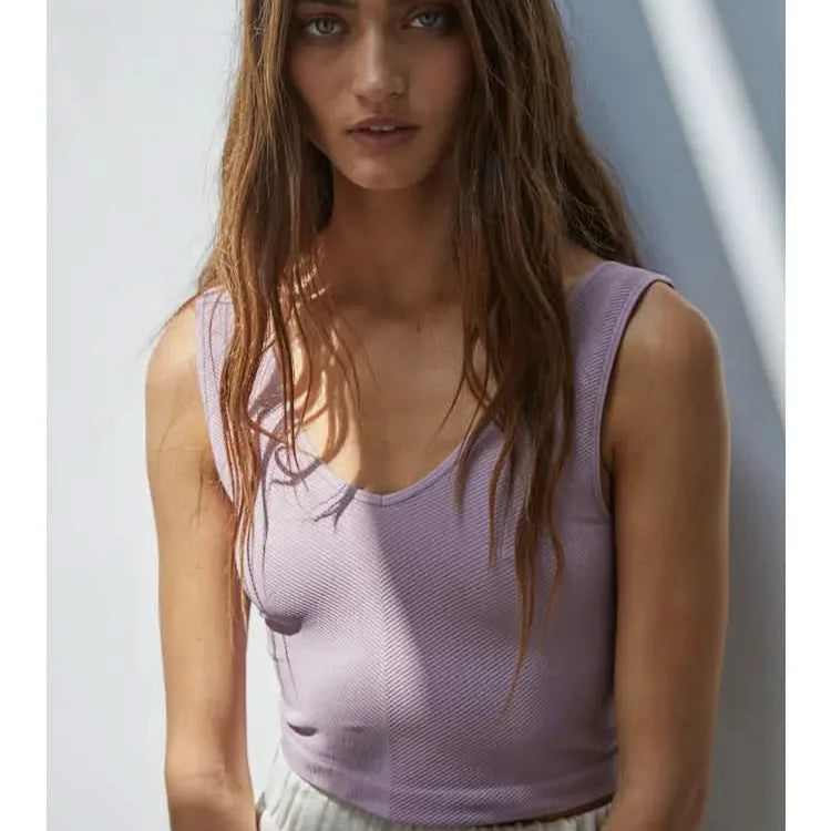 Woman wearing a purple knit seamless chevron design with a sleeveless U-V neckline tank top behind a white wall.