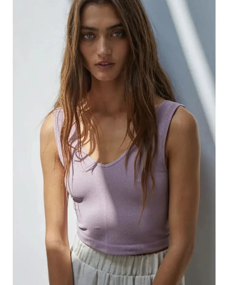 Woman wearing a purple knit seamless chevron design with a sleeveless U-V neckline tank top behind a white wall.
