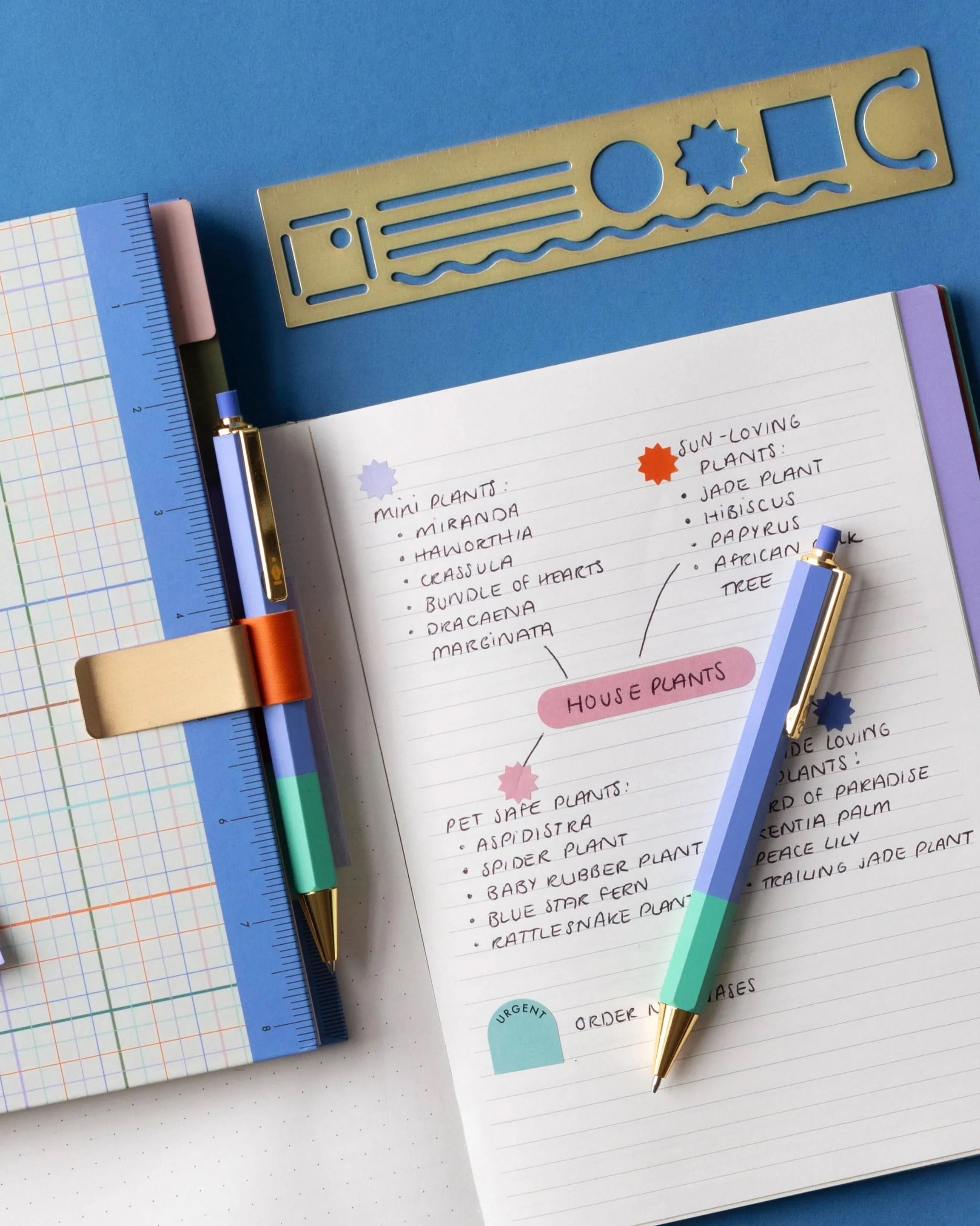 Mechanical pencil and pen in use laying on notebook and in pen holder on blue background
