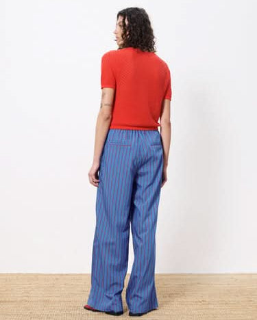 Woman facing away wearing red top and blue pants with red vertical stripes all over