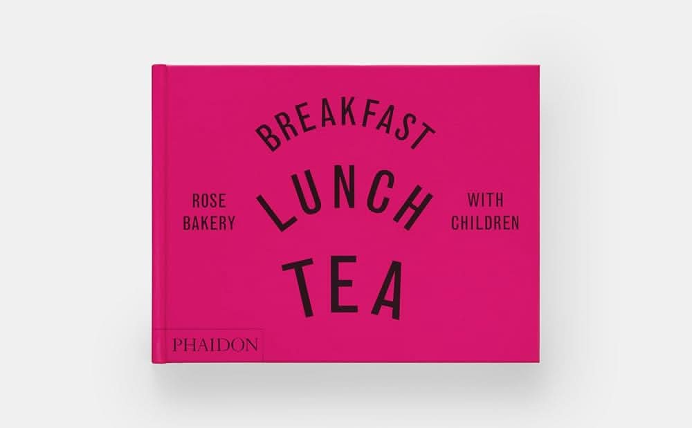 Bright pink, horizontal, hardcover book with black lettering “breakfast lunch tea with children from rose bakery”