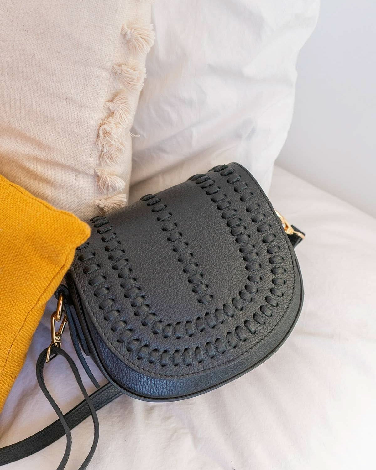 Black colored leather crossbody bag with magnetic front clap and leather woven geometric design and gold Metal details