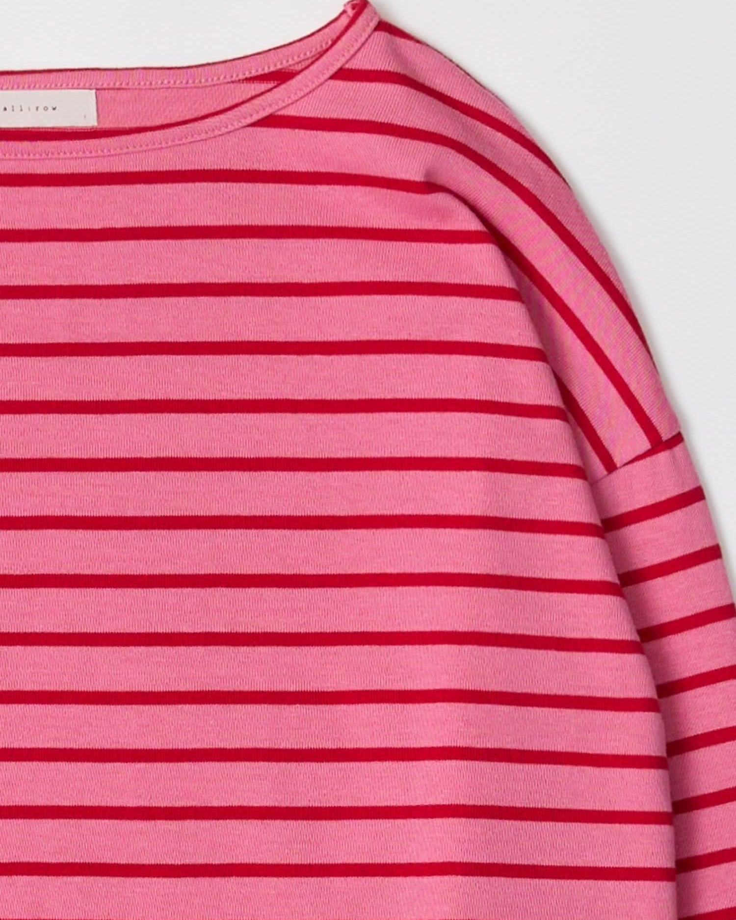Close up of long sleeve, pink, pullover sweater with thin red horizontal stripes