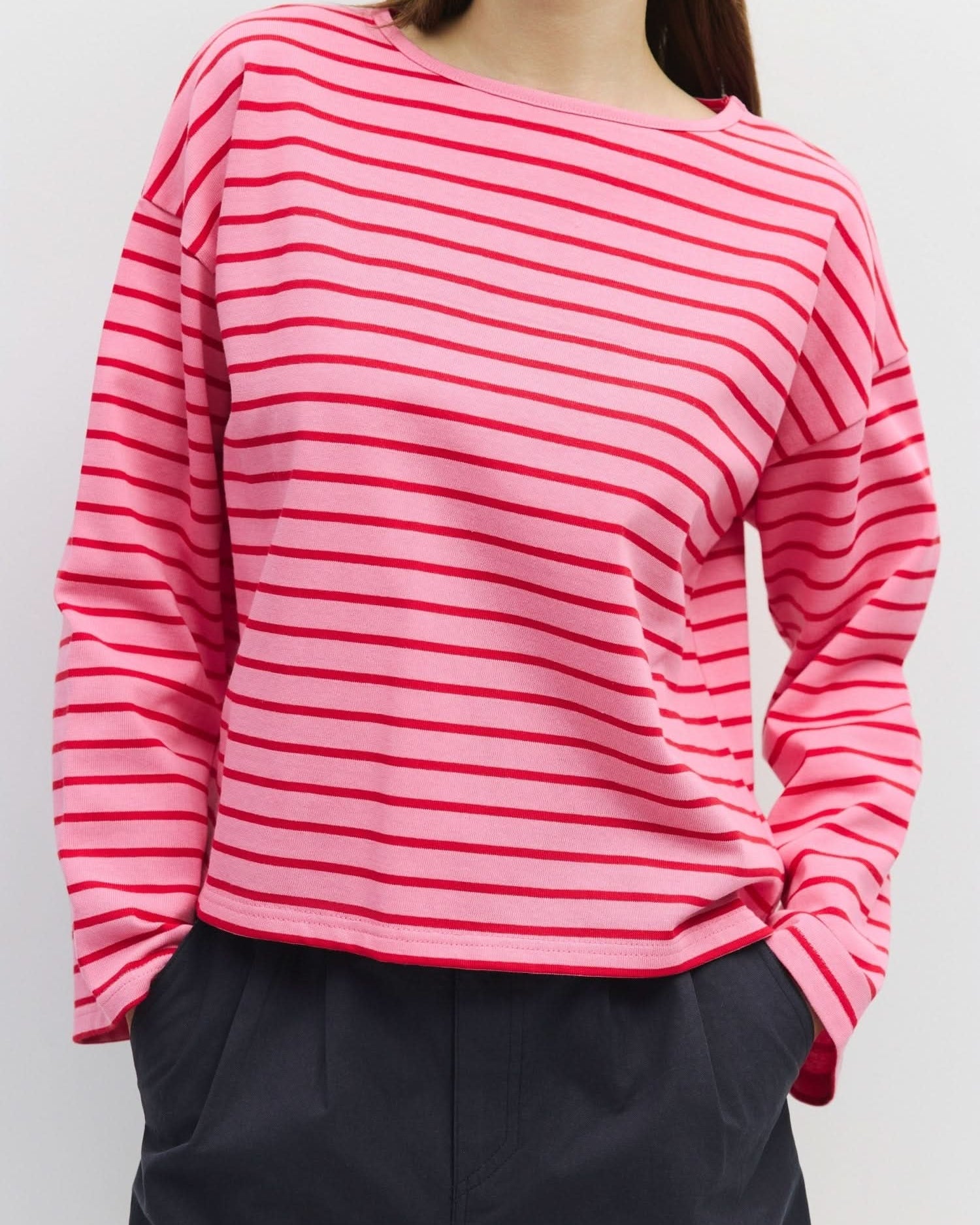 Woman wearing long sleeve, pink, pullover sweater with thin red horizontal stripes