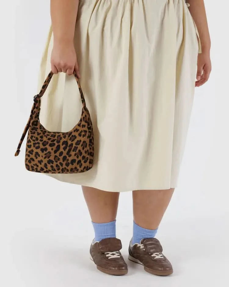 Woman wearing a yellow skirt holding a small over the shoulder leopard purse in hand behind a white background.