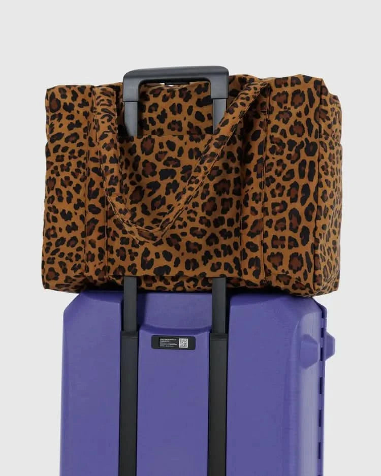 Large leopard over the shoulder carry-on tote bag on a purple suitcase behind a white background.