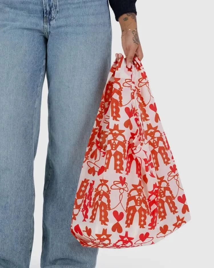 Woman carrying Pinkish white baby baggu reuseable grocery bag with red cowgirl print throughout the bag