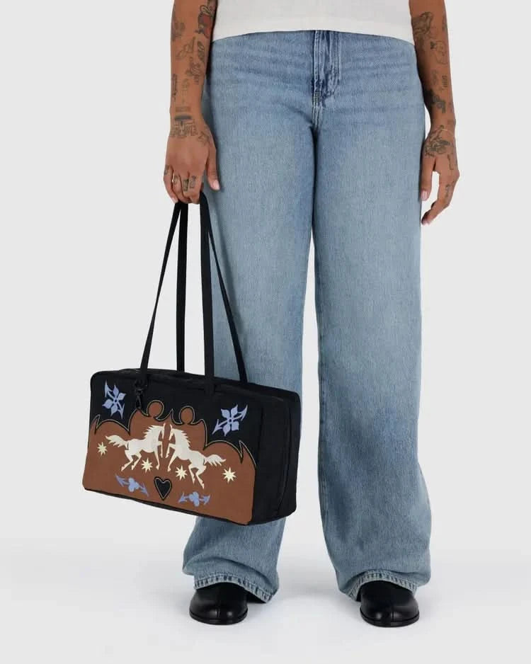 Someone carrying Brown, black, light blue, and white nylon BAGGU western bowler bag. With horses in the front, Four charm loops and a swivel clasp to let you accessorize