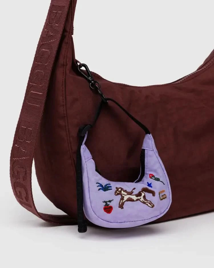 Purple embroidered crescent bag charm with horses, flowers, plants, and a snake clipped on to a brown crescent baggu bag