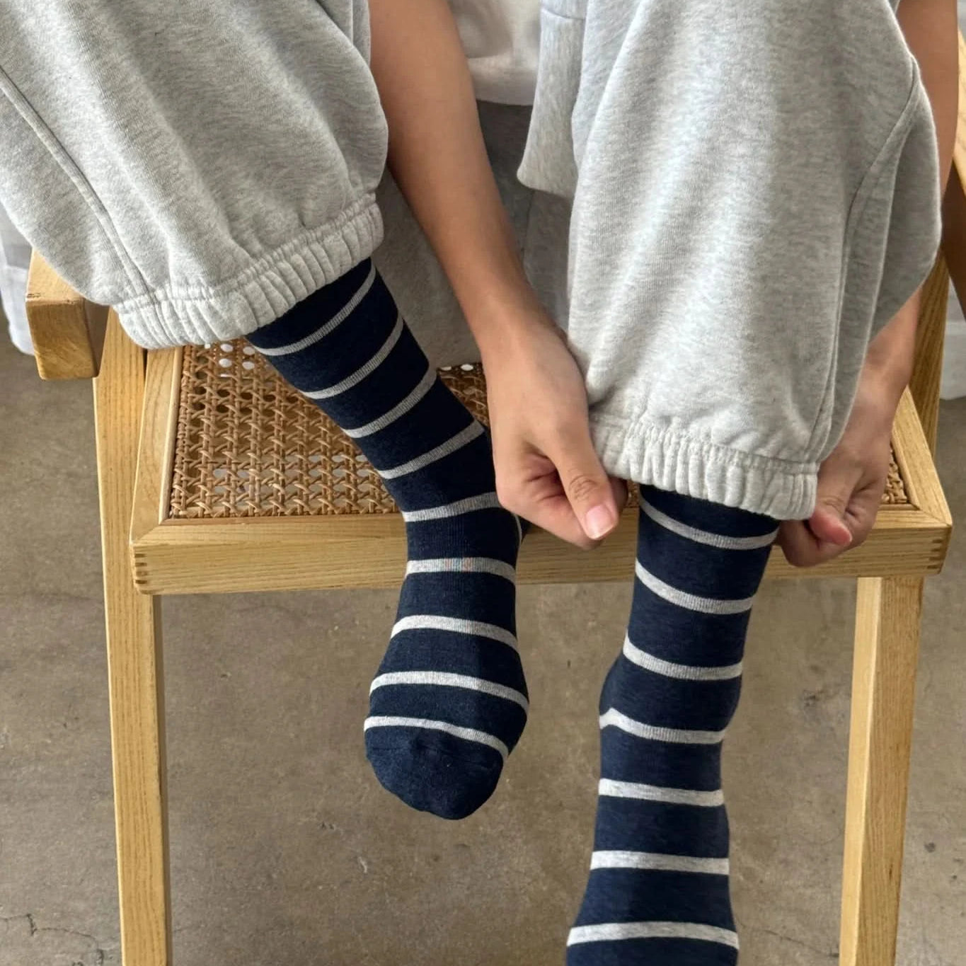Person wearing gray sweatpants and navy blue striped socks sitting on a wooden chair.