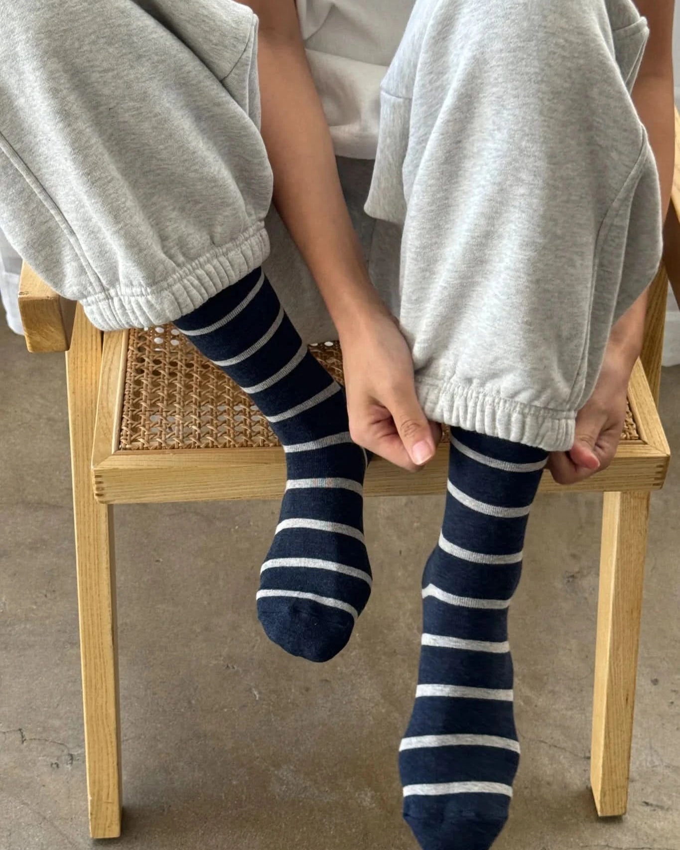 Person wearing gray sweatpants and navy blue striped socks sitting on a wooden chair.
