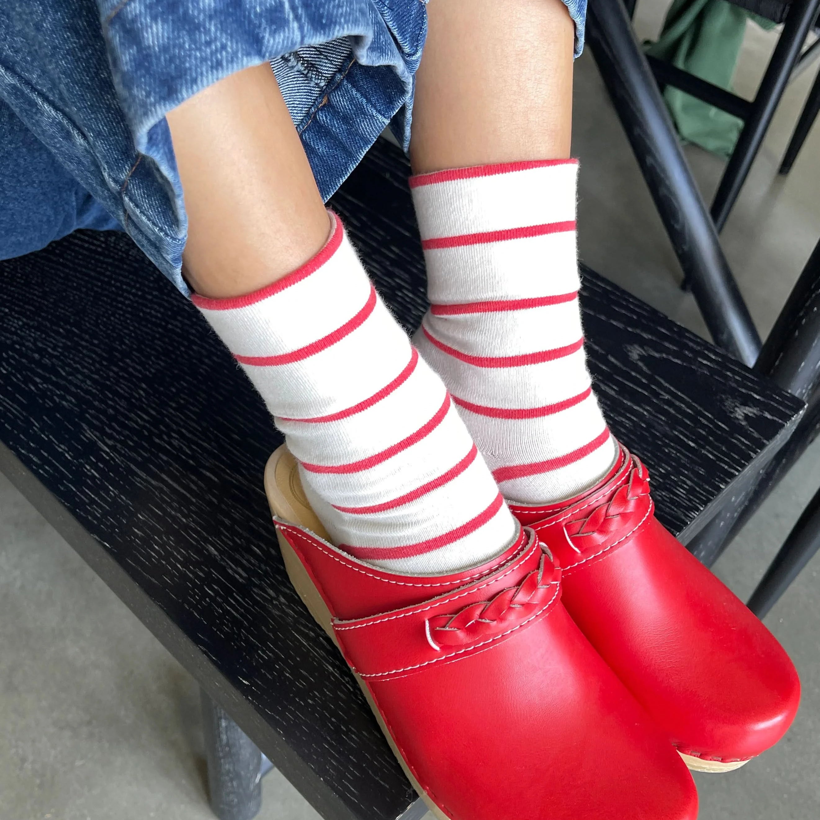 Person wearing red shoes and white socks with red stripes, sitting on a black chair.