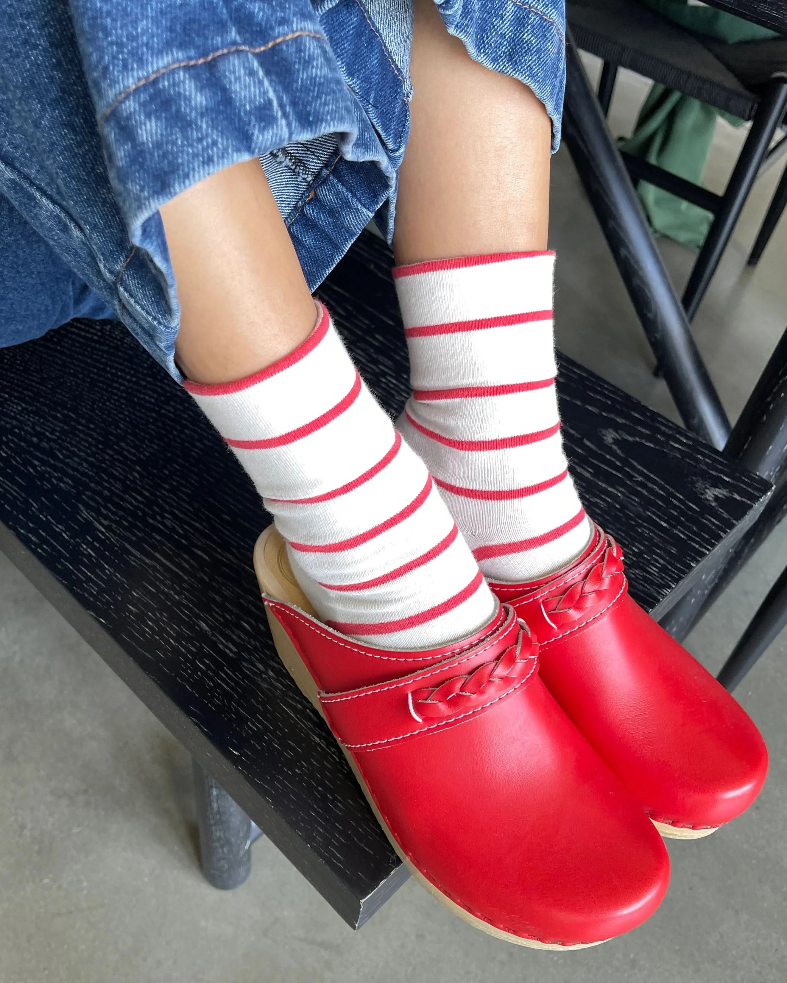 Person wearing red shoes and white socks with red stripes, sitting on a black chair.