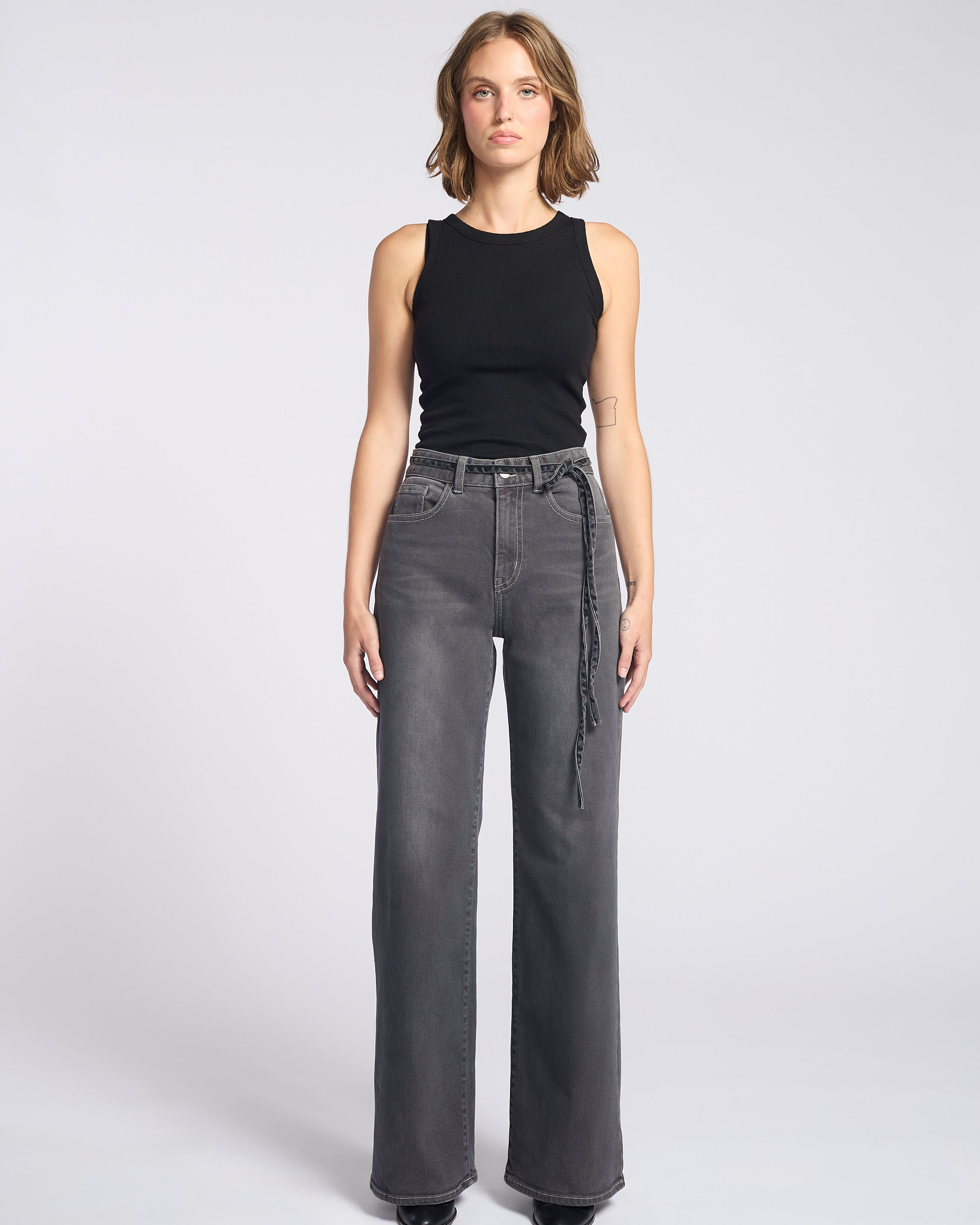 Woman wearing dark grey jeans with string tie belt and black tank top