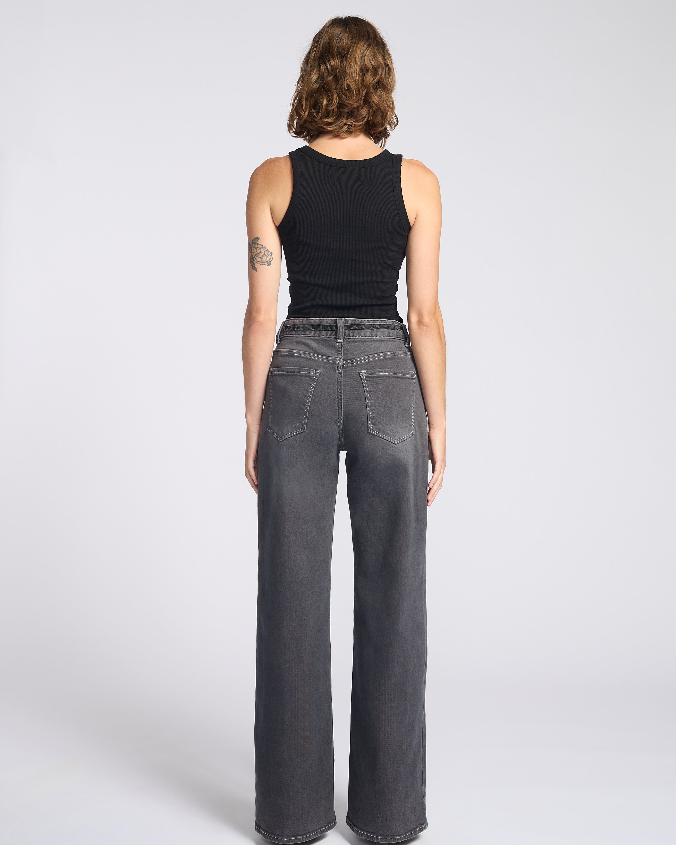 Woman wearing dark grey jeans with string tie belt and black tank top