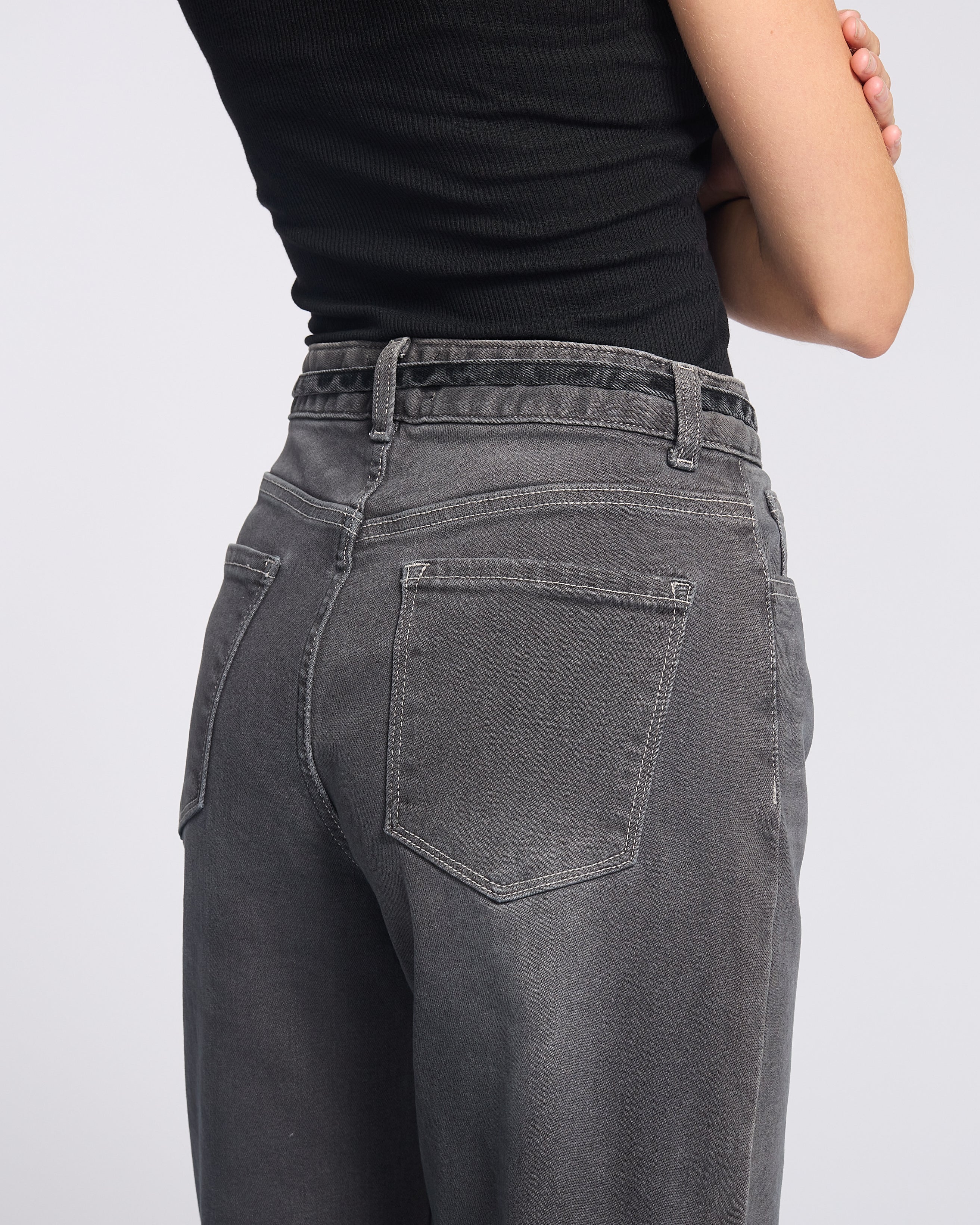 Woman wearing dark grey jeans with string tie belt and black tank top