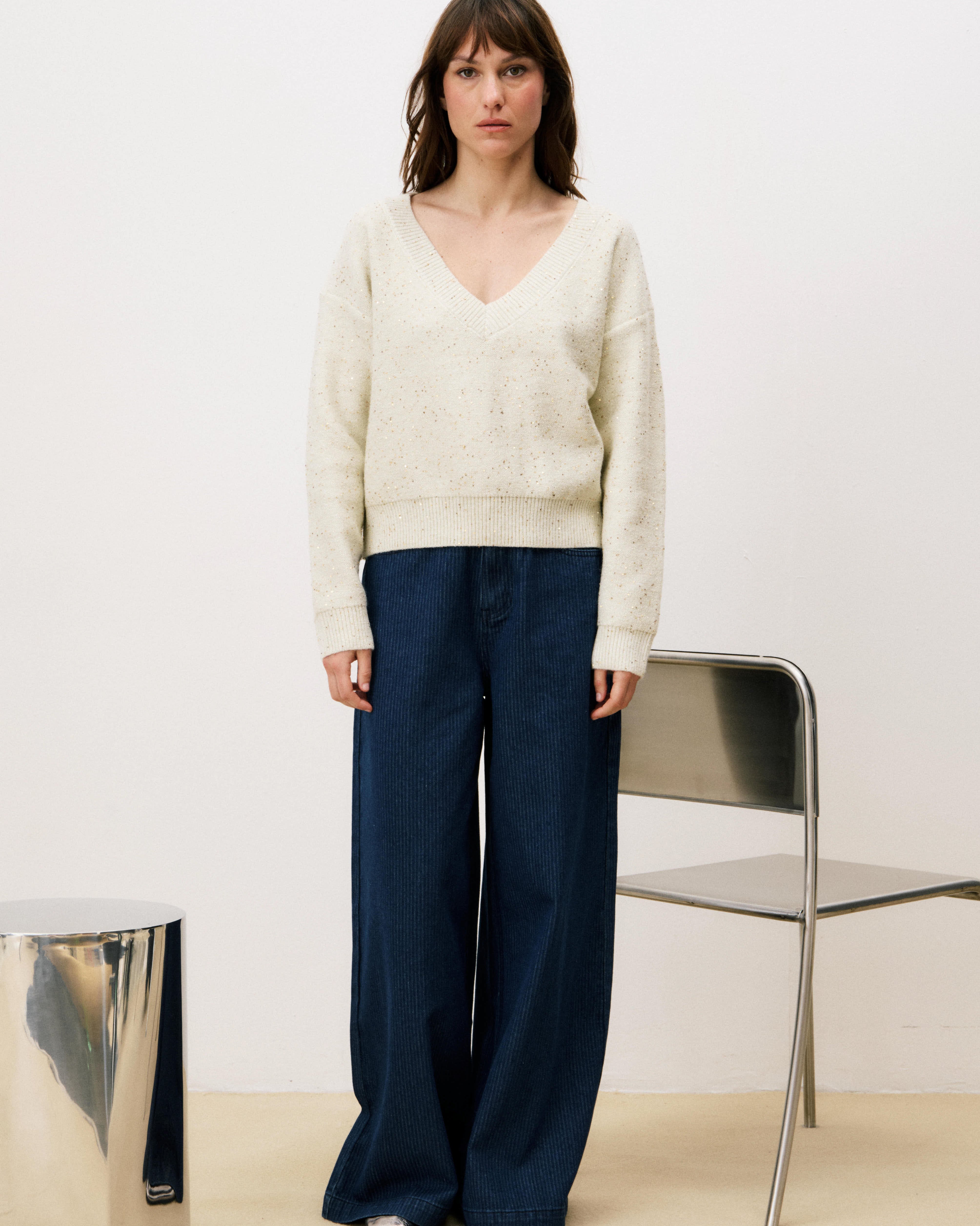 Woman wearing a cream sweater and navy pants against a white background