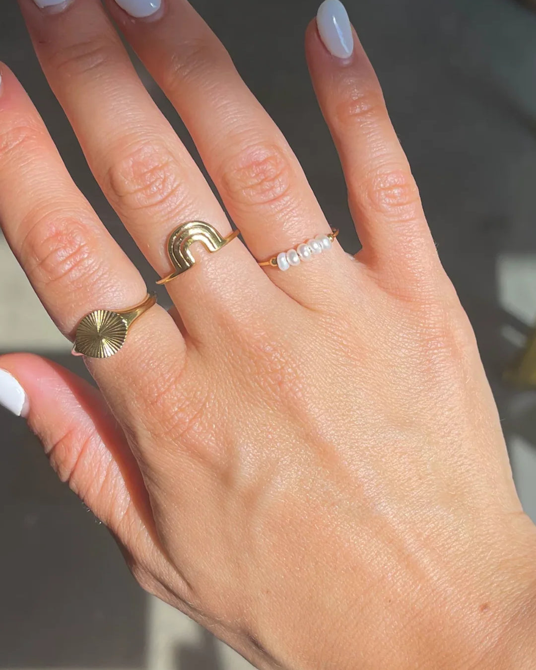 Hand wearing multiple gold rings including Polly pearl ring with a white nails