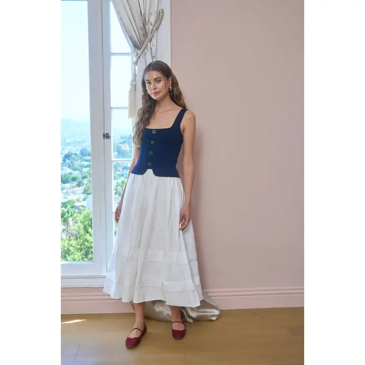 Woman wearing a blue top and white skirt standing in a room with large windows.
