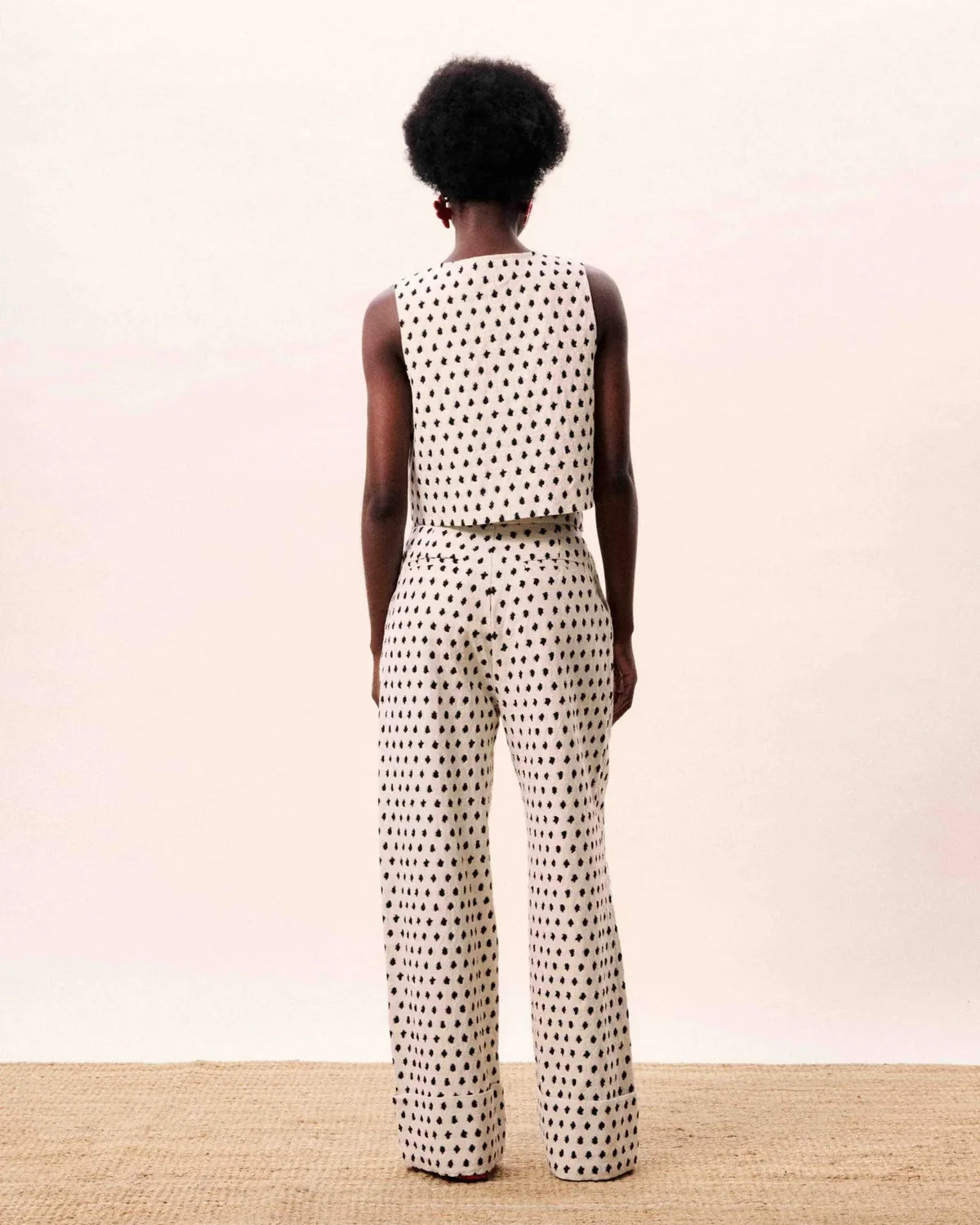 Person wearing a patterned sleeveless top and pants on a plain background