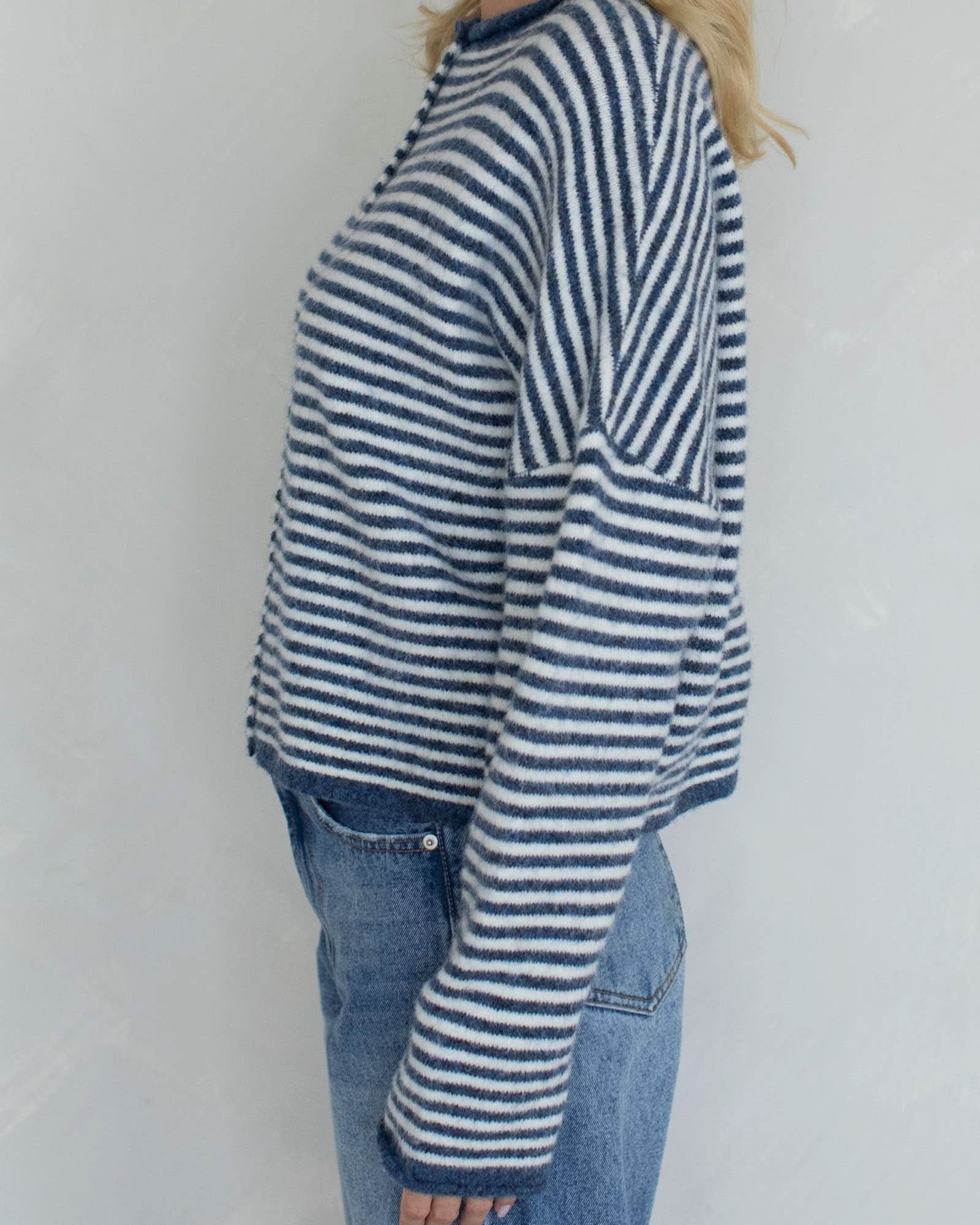 Person wearing a blue and white striped sweater and jeans against a plain background