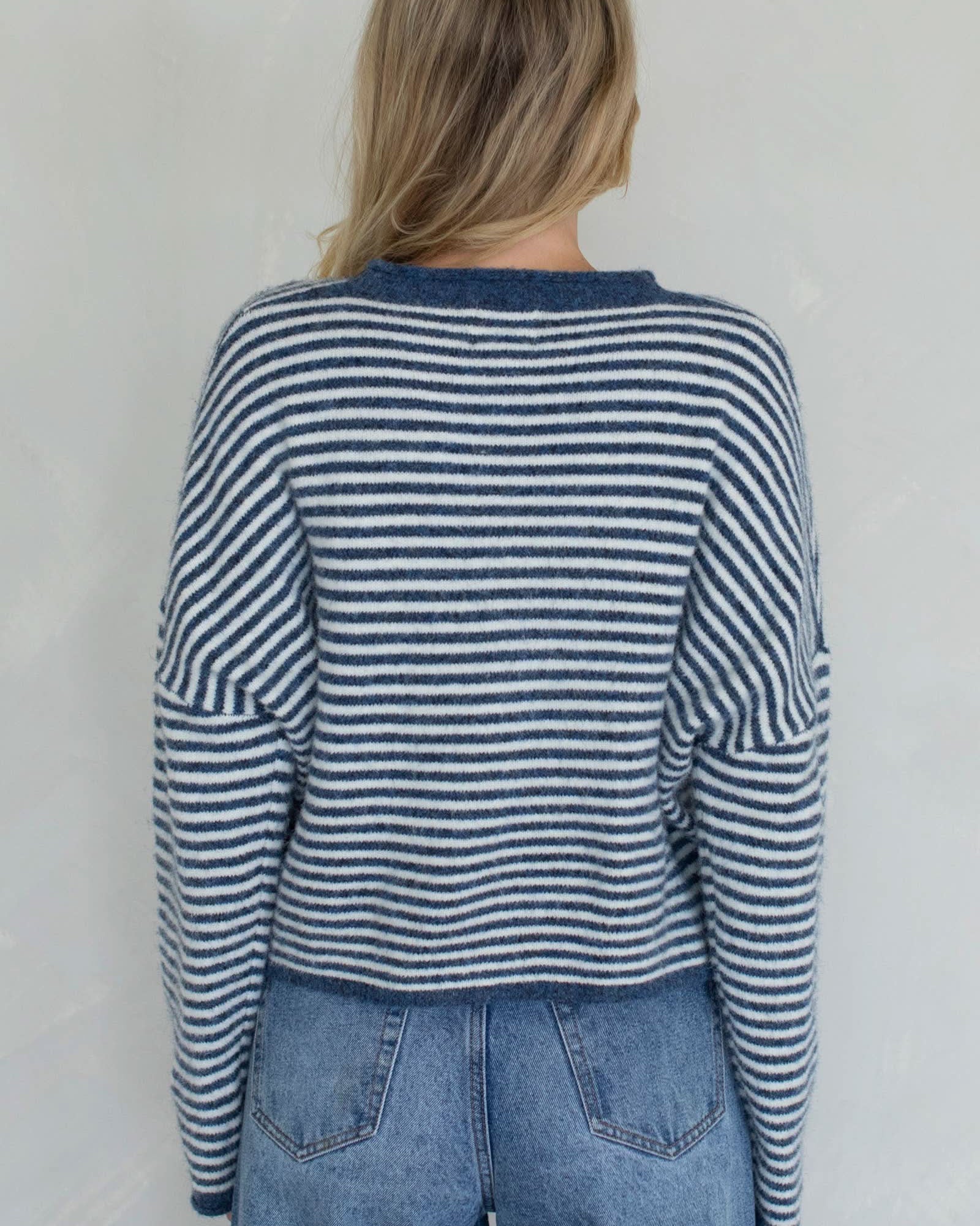 Person wearing a blue and white striped sweater and jeans against a plain background