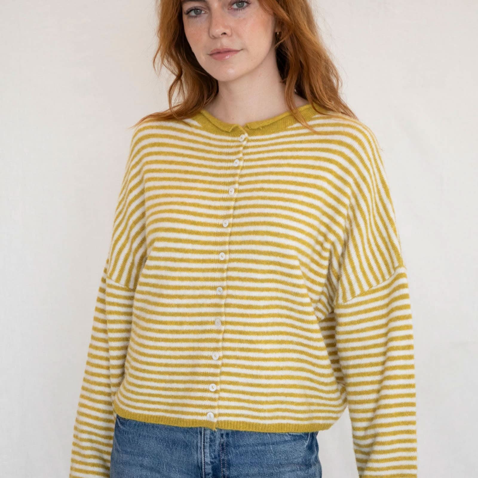 Woman wearing a yellow and white striped shirt with blue jeans against a plain background