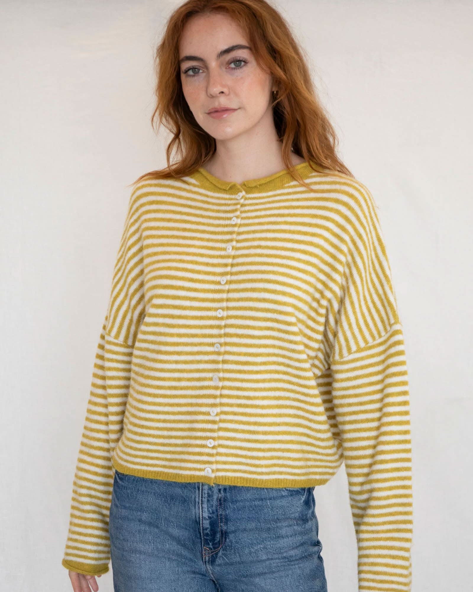 Woman wearing a yellow and white striped shirt with blue jeans against a plain background