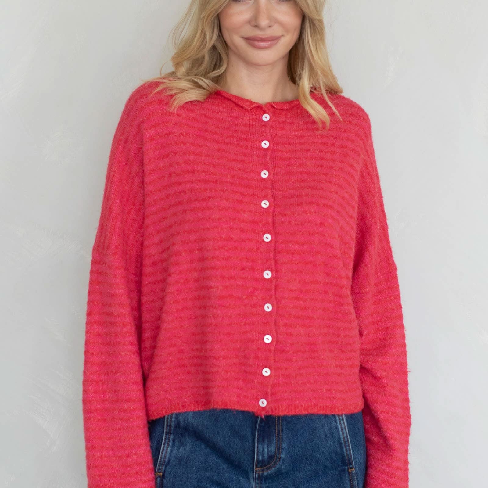 Woman wearing a red textured shirt with white buttons against a plain background