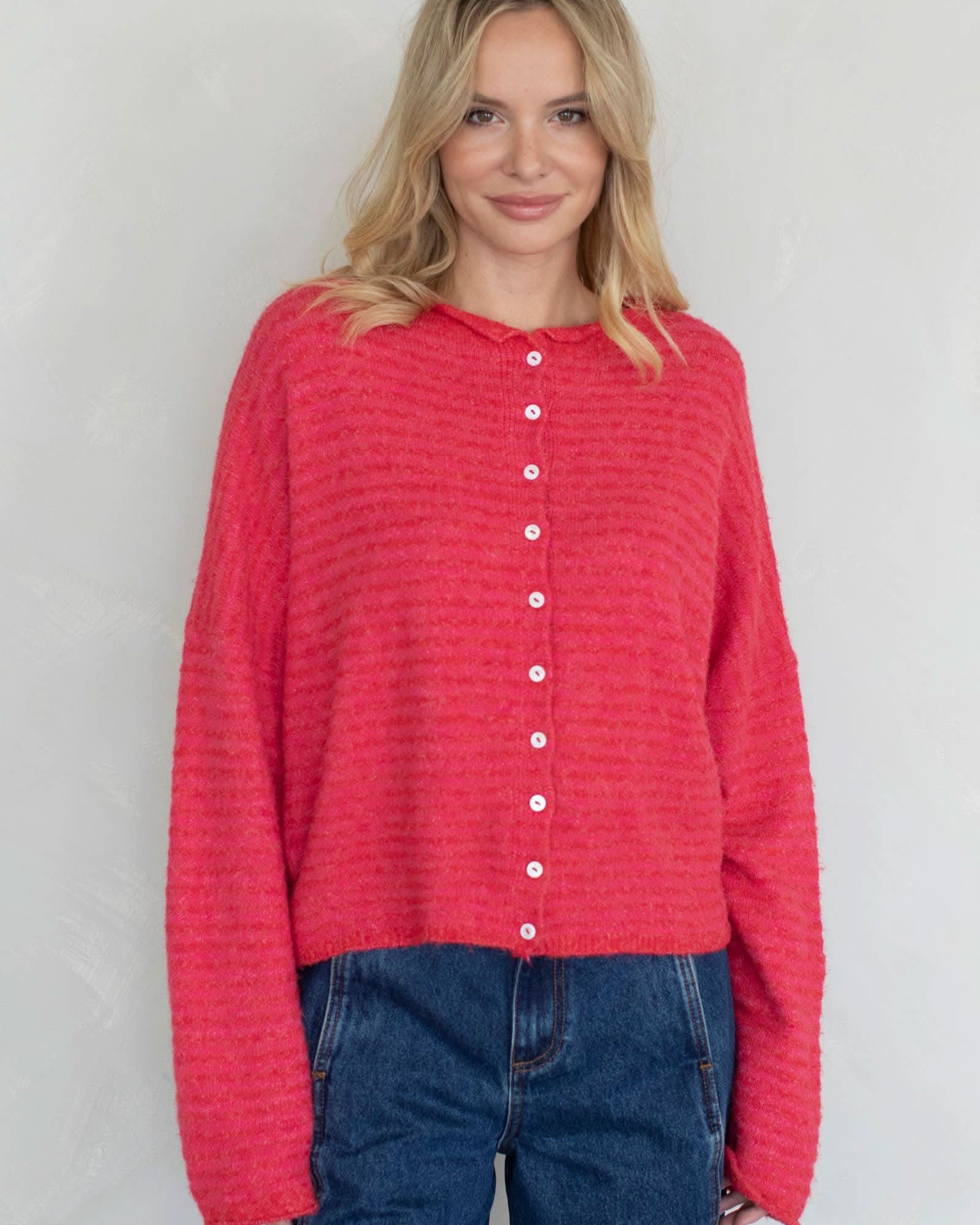 Woman wearing a red textured shirt with white buttons against a plain background