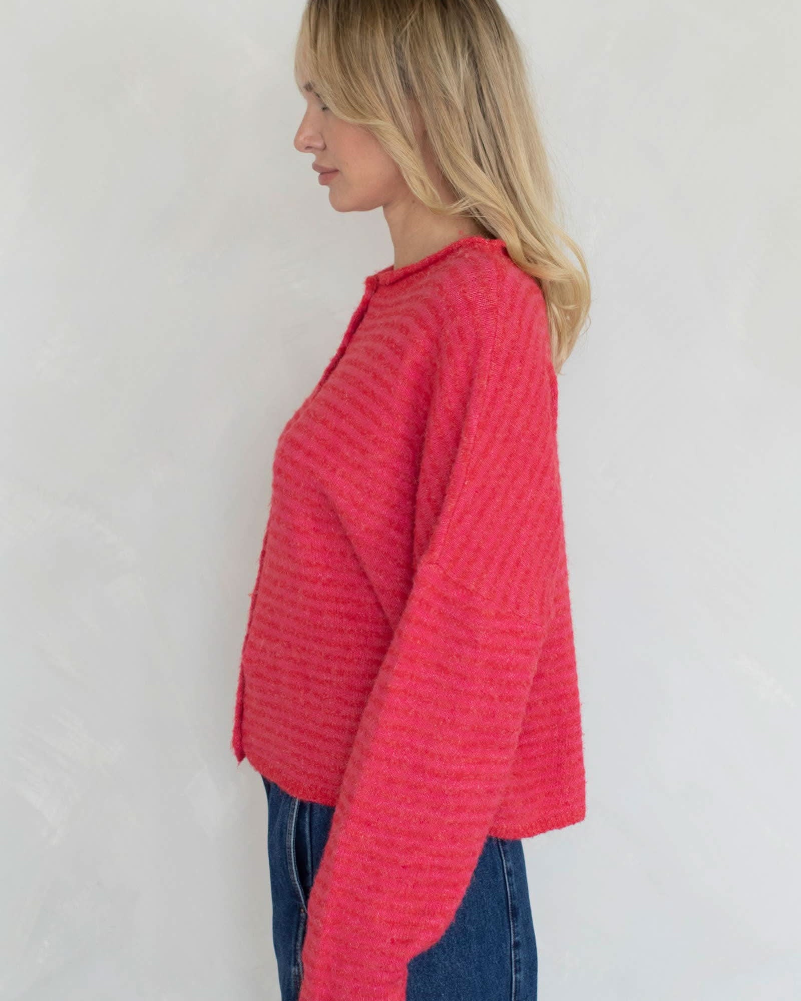 Woman wearing a red knitted sweater and blue jeans against a white background