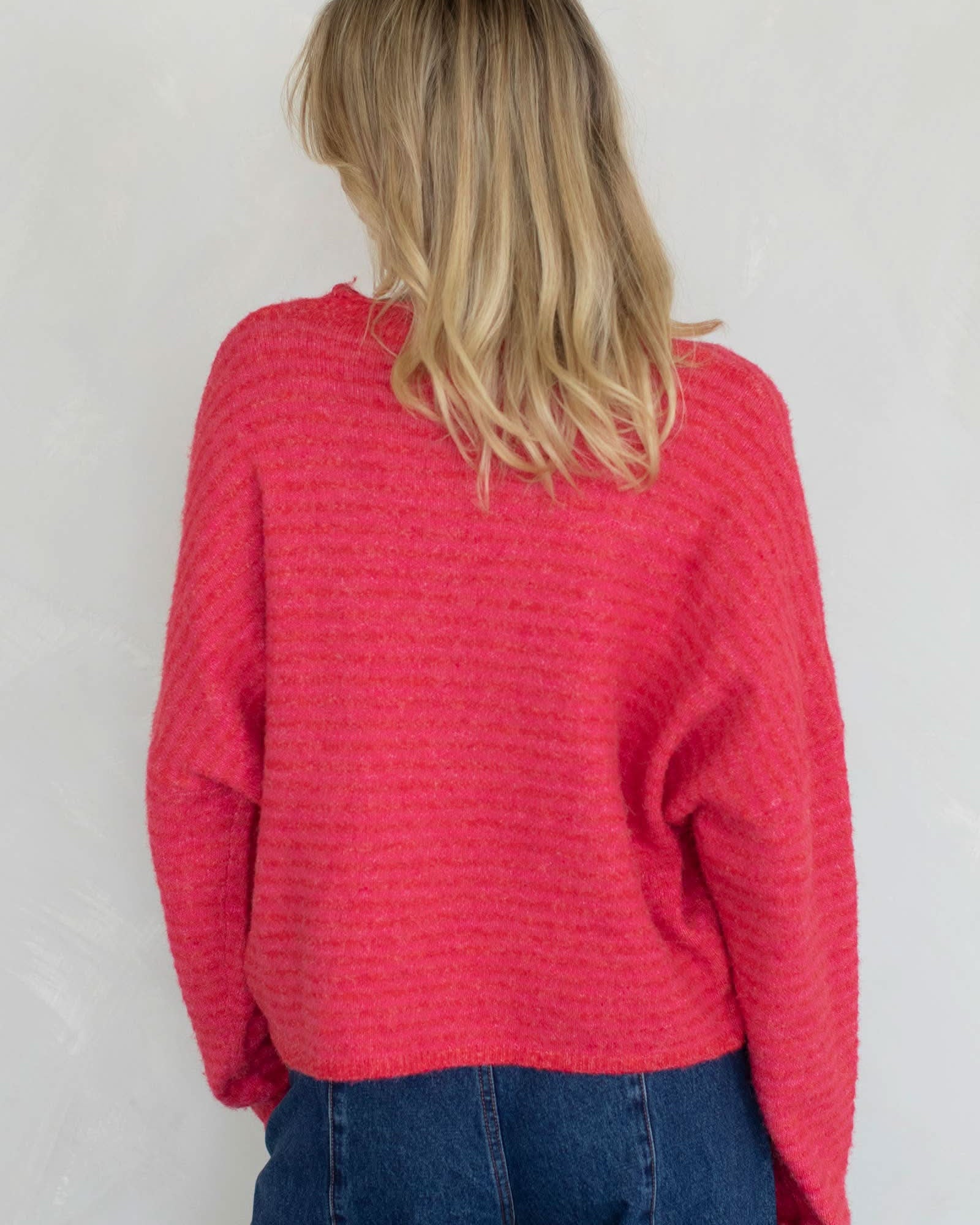 Person wearing a red textured sweater and blue jeans against a plain background