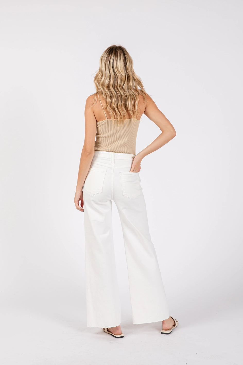 Woman wearing a beige top and white pants on a white background