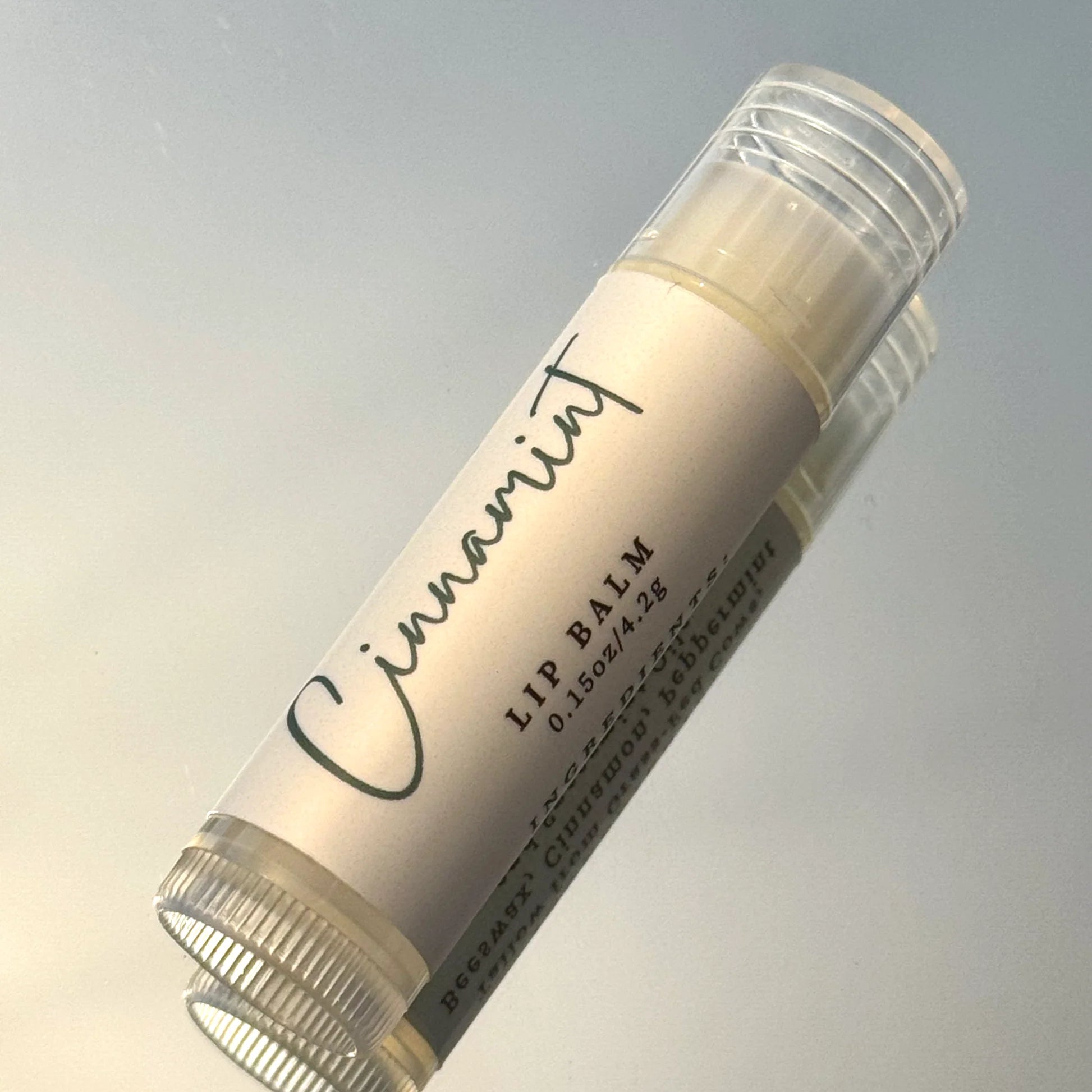 Lip balm stick with 'Cinnamint' branding on a gradient background