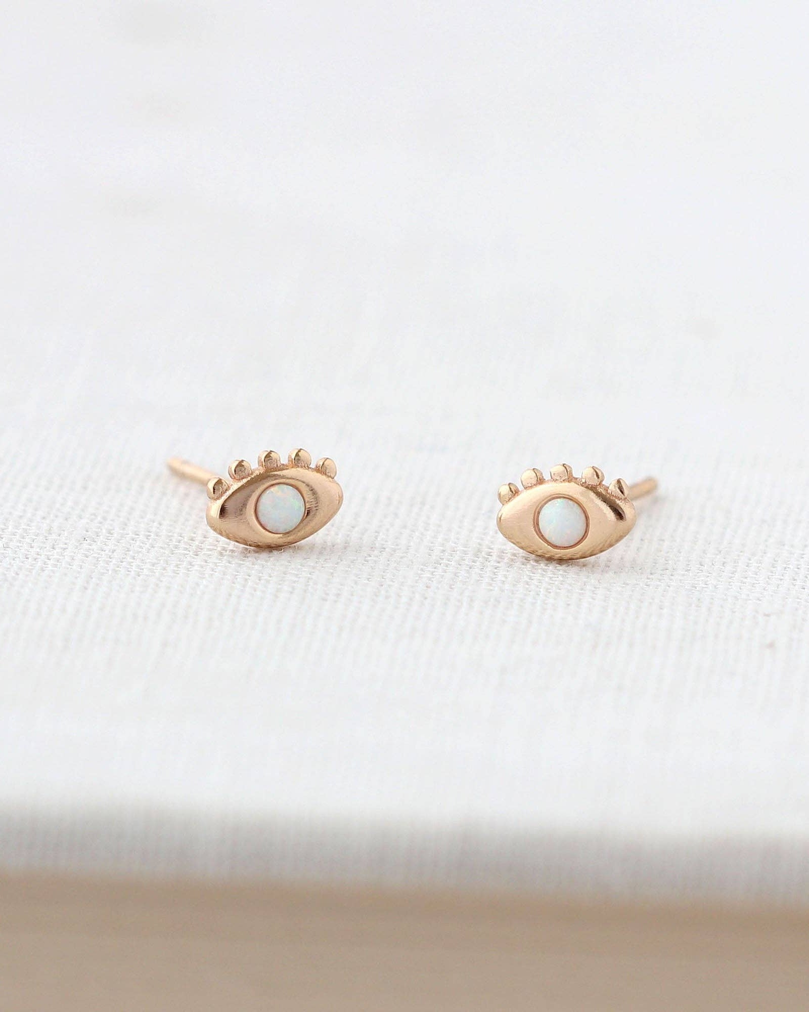 Rose gold eye-shaped earrings on a white fabric background