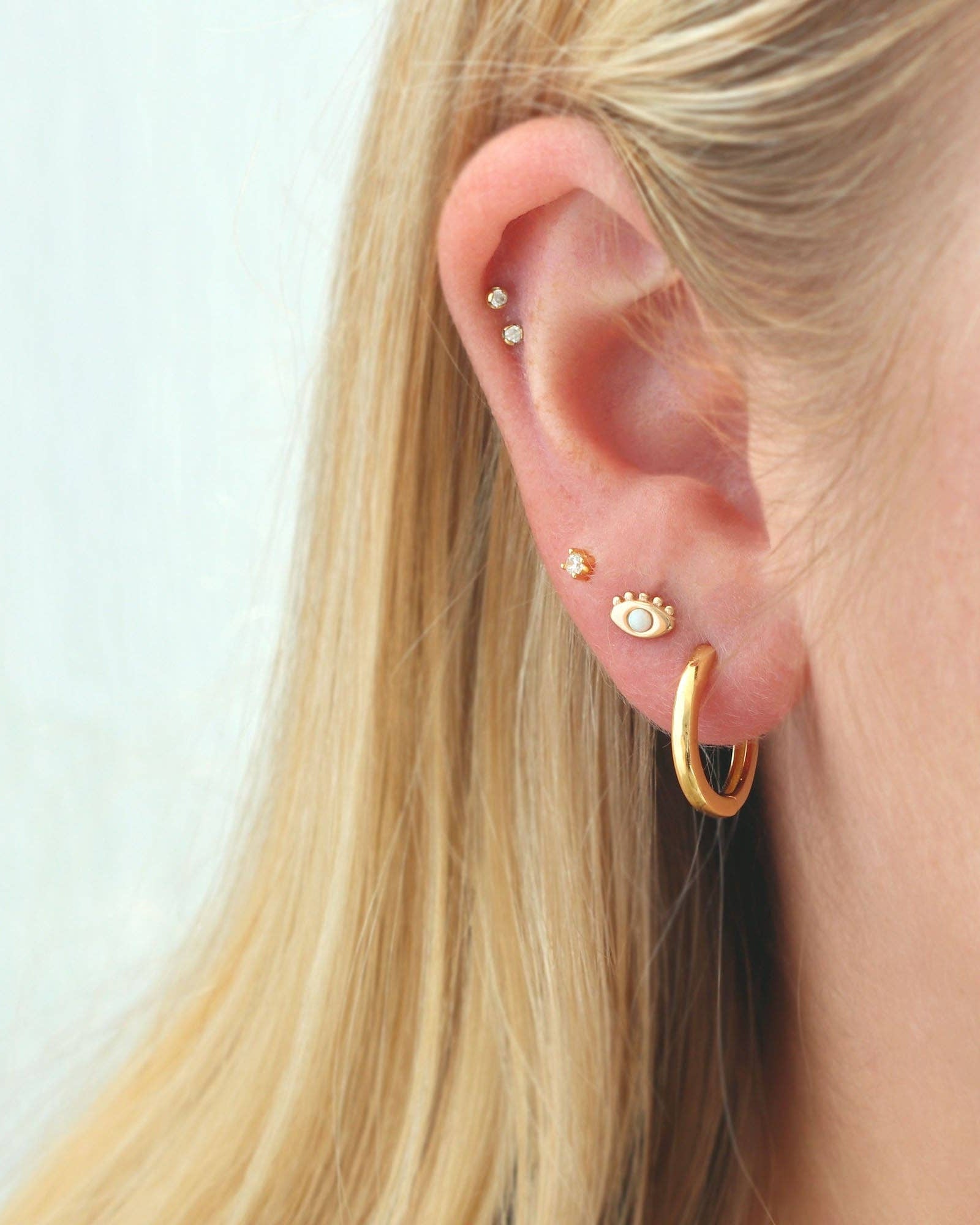 Close-up of an ear with gold hoop earrings and small studs on a light background