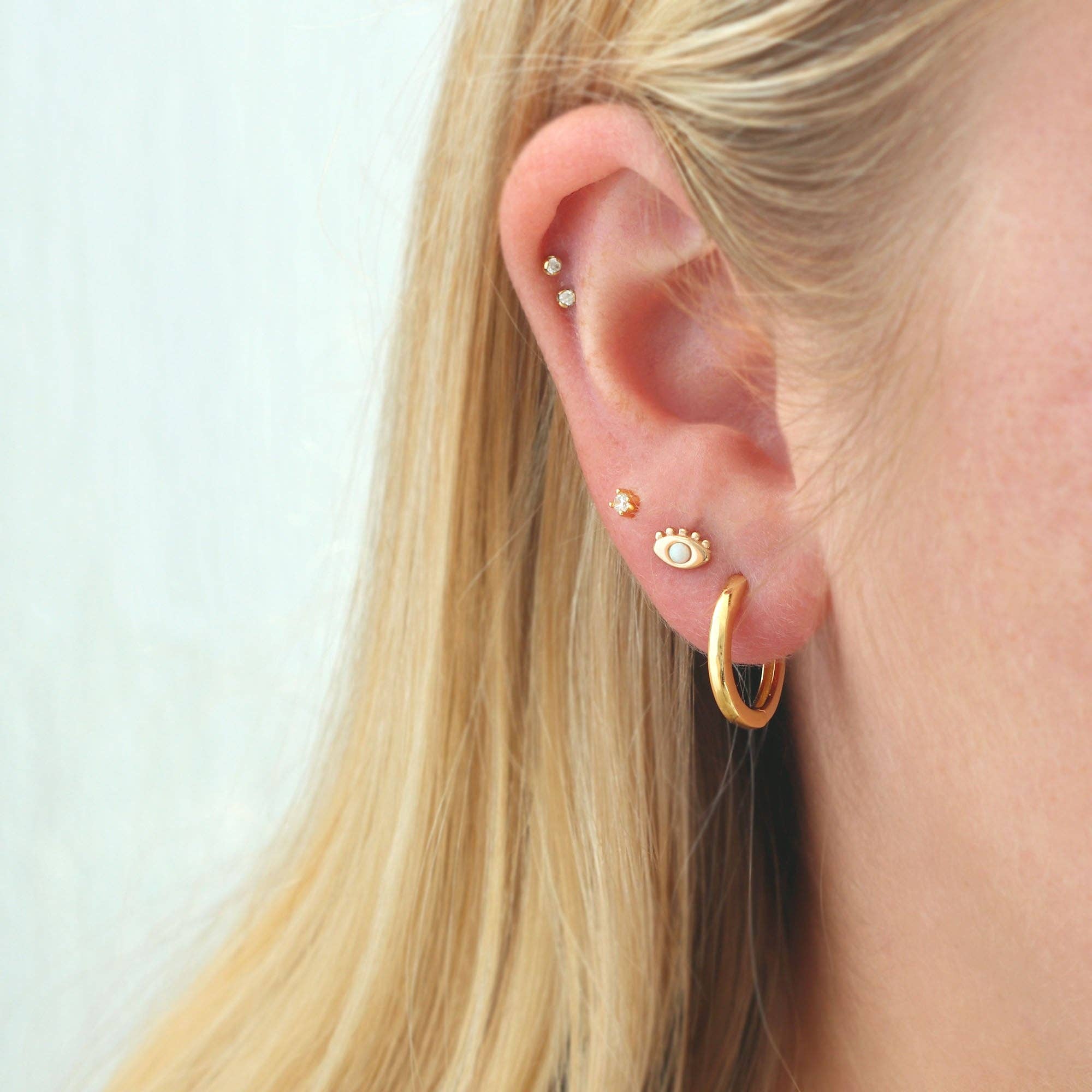 Close-up of an ear with gold hoop earrings and small studs on a light background
