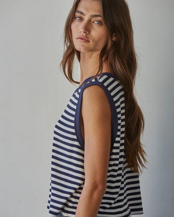 Woman wearing a striped tank top and jeans against a plain background