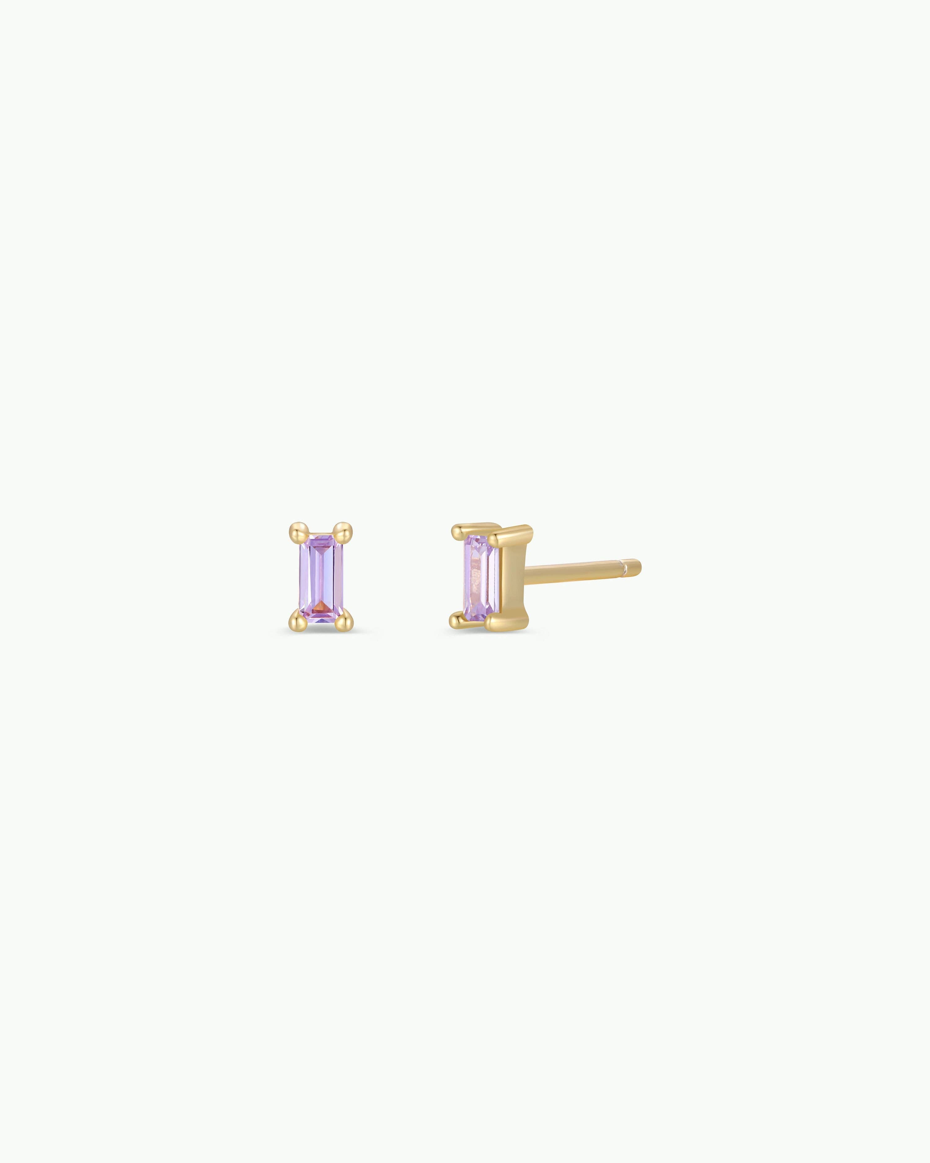 Gold earrings with purple gemstones on a white background