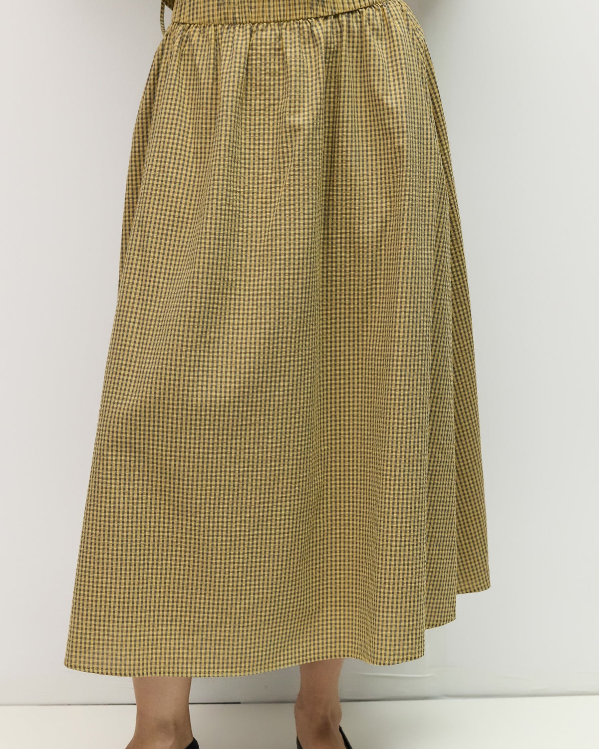 Person wearing a yellow checkered skirt against a white background