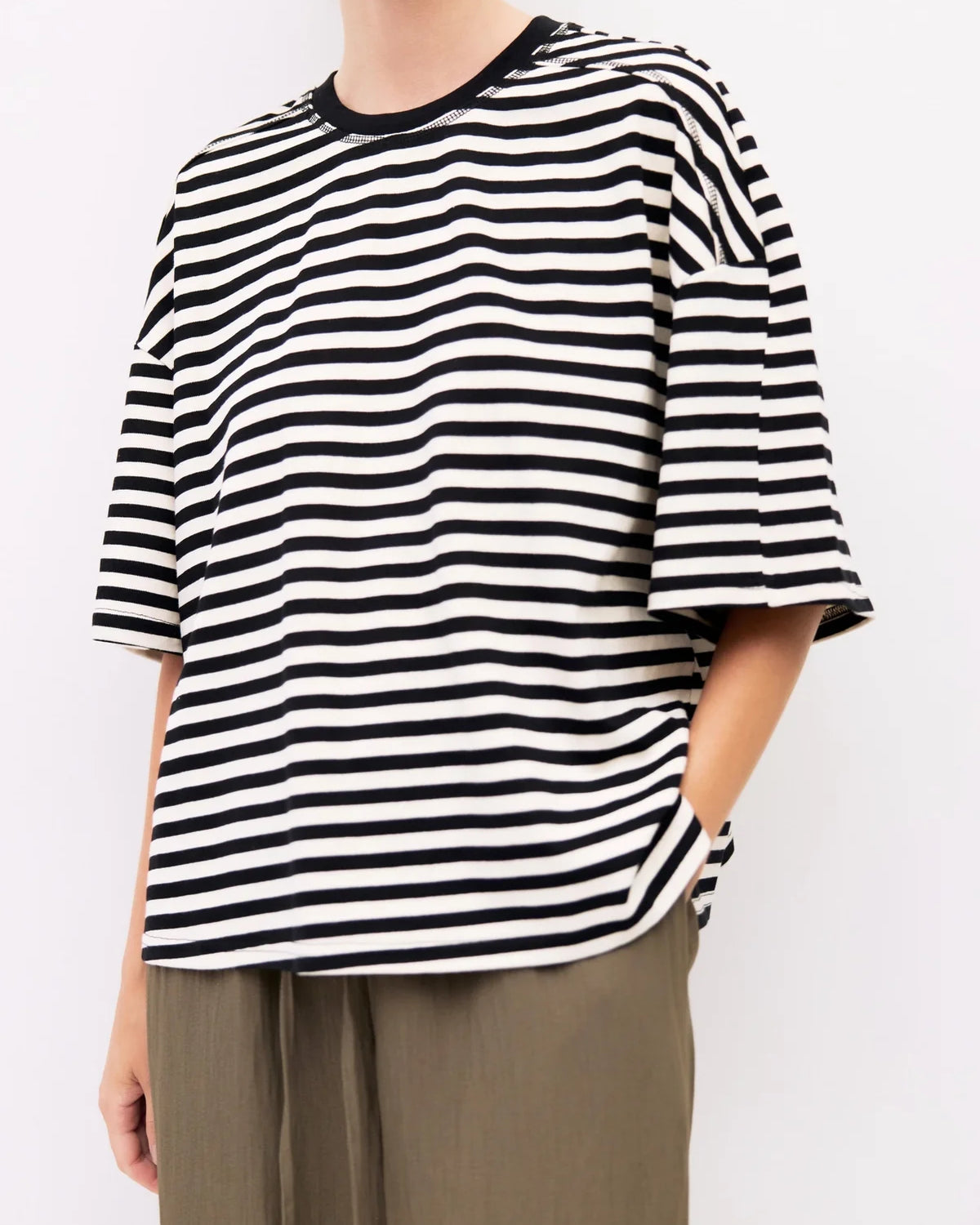 A person wearing an oversized black and white horizontally striped short-sleeve top with a black crew neck, paired with olive green drawstring pants, against a plain white background.