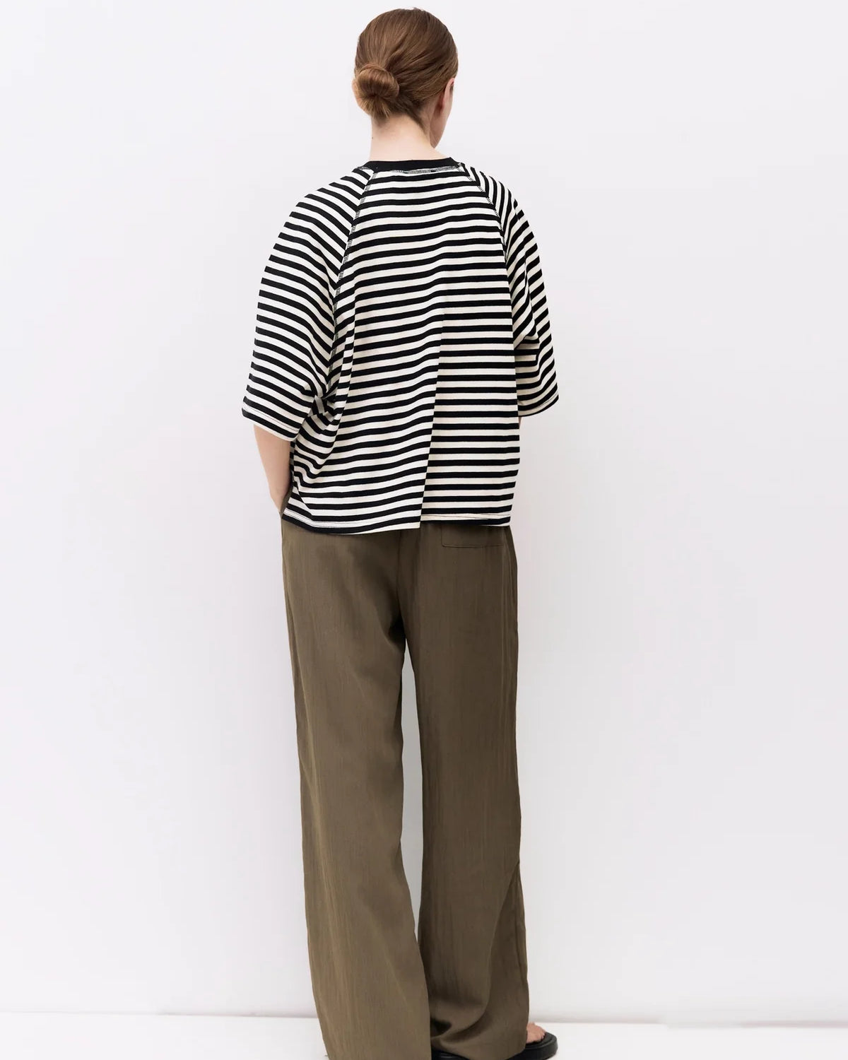 Person wearing a black and white striped shirt and brown pants on a white background